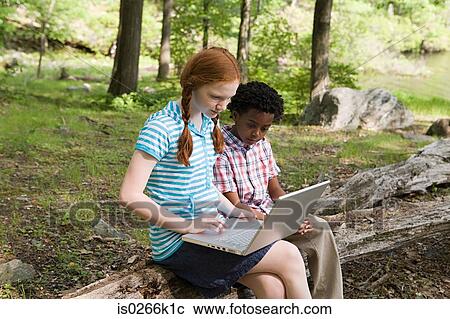 Stock Image - Friends using a laptop in a forest. Fotosearch