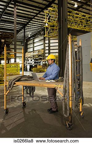 Stock Photo - Man in warehouse with laptop. Fotosearch
