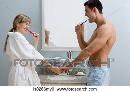 Stock Image - A couple holding hands whilst they brush their teeth. Fotosearch