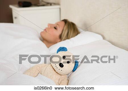Stock Image - Woman in bed with teddy bear. Fotosearch