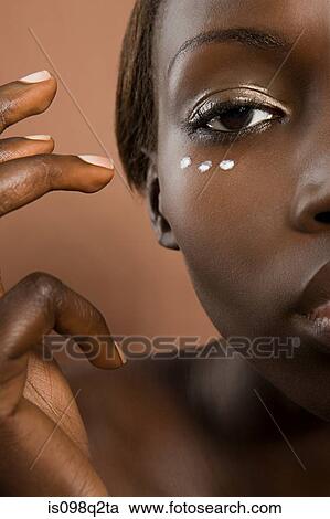 Stock Image - Young woman applying moisturiser to face. Fotosearch