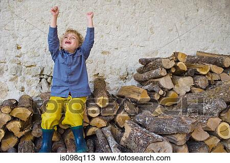 Stock Image - A boy sitting on a stack of logs. Fotosearch
