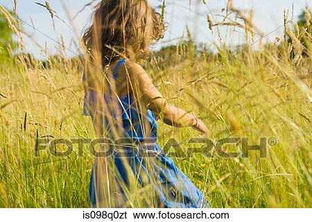 A girl walking through a field of long grass View Large Photo Image Stock Photograph - A girl walking through a field of long grass. Fotosearch