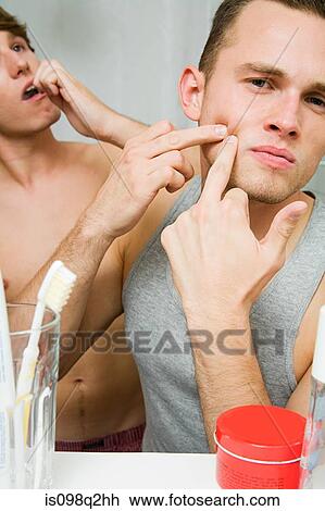 Stock Image - A man squeezing a spot in the mirror. Fotosearch