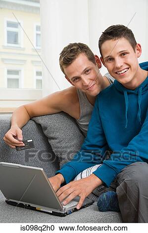 Stock Image - Portrait of a gay couple with a laptop and credit card. Fotosearch