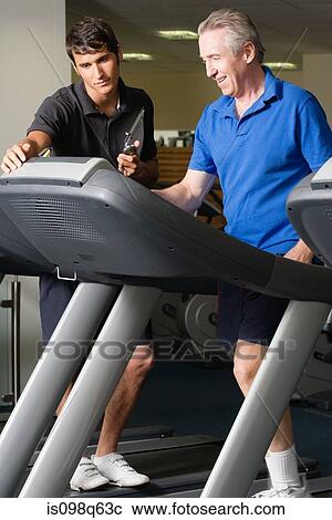 A personal trainer helping a man on a treadmill View Large Photo Image Stock Image - A personal trainer helping a man on a treadmill. Fotosearch