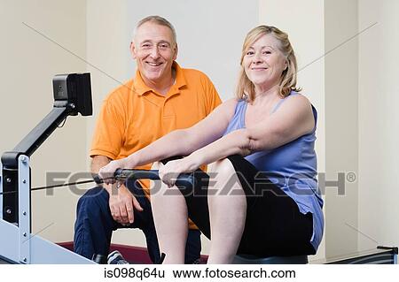 Stock Photograph - Personal trainer helping a woman on a rowing machine. Fotosearch