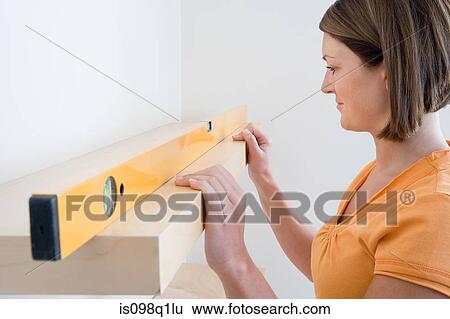 Stock Photograph - A young woman checking a shelf with a spirit level. Fotosearch