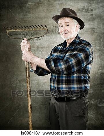 Portrait of a farmer holding a rake View Large Photo Image Stock Photo - Portrait of a farmer holding a rake. Fotosearch