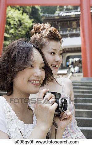 Stock Image - Young women at shrine with camera. Fotosearch