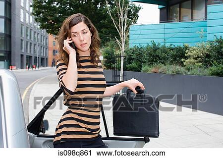Stock Image - Woman on cellphone by car. Fotosearch