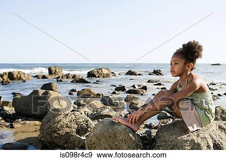 Girl sitting on rocks at the beach View Large Photo Image Stock Photo - Girl sitting on rocks at the beach. Fotosearch