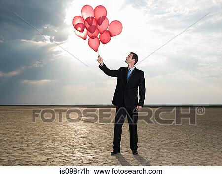 Stock Image - Businessman holding a bunch of red balloons. Fotosearch