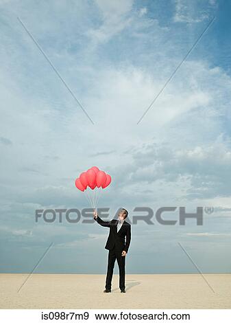 Businessman holding a bunch of red balloons View Large Photo Image Stock Photo - Businessman holding a bunch of red balloons. Fotosearch