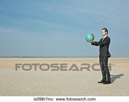 Stock Image - Businessman holding a globe in desert. Fotosearch