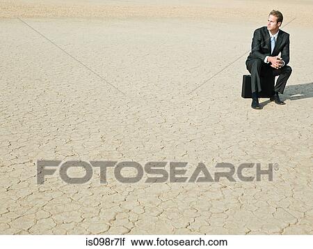 Businessman sitting on a briefcase in the desert View Large Photo Image Stock Image - Businessman sitting on a briefcase in the desert. Fotosearch
