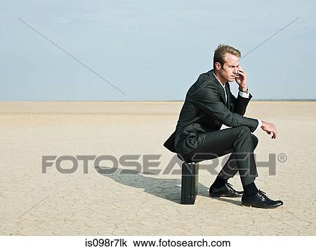 Businessman sitting on a briefcase in the desert View Large Photo Image Stock Image - Businessman sitting on a briefcase in the desert. Fotosearch