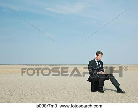 Businessman sitting on a briefcase in the desert View Large Photo Image Stock Image - Businessman sitting on a briefcase in the desert. Fotosearch