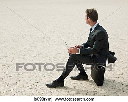 Businessman sitting on a briefcase in the desert View Large Photo Image Stock Image - Businessman sitting on a briefcase in the desert. Fotosearch