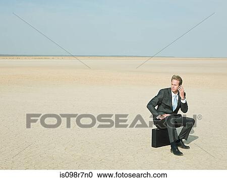 Businessman sitting on a briefcase in the desert View Large Photo Image Stock Image - Businessman sitting on a briefcase in the desert. Fotosearch