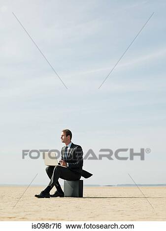 Businessman sitting on a briefcase in the desert View Large Photo Image Stock Photograph - Businessman sitting on a briefcase in the desert. Fotosearch