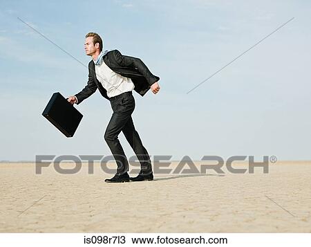 Stock Image - Businessman walking in a windy desert. Fotosearch
