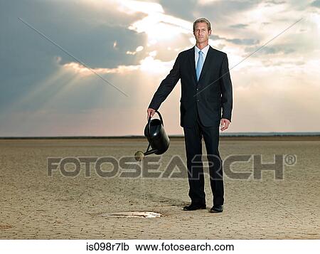 Businessman with a watering can in the desert View Large Photo Image Stock Image - Businessman with a watering can in the desert. Fotosearch