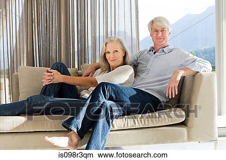 Picture - Middle aged couple reclining on couch. Fotosearch
