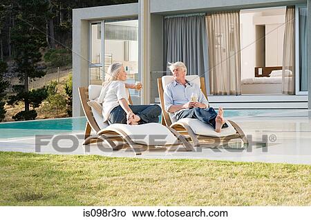 Picture - Middle aged couple relaxing on deck chairs by the pool. Fotosearch
