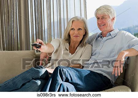 Middle aged couple sitting on couch together watching TV View Large Photo Image Stock Photograph - Middle aged couple sitting on couch together watching TV. Fotosearch
