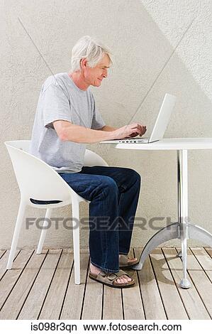 Middle aged man sitting on desk and using laptop View Large Photo Image Picture - Middle aged man sitting on desk and using laptop. Fotosearch