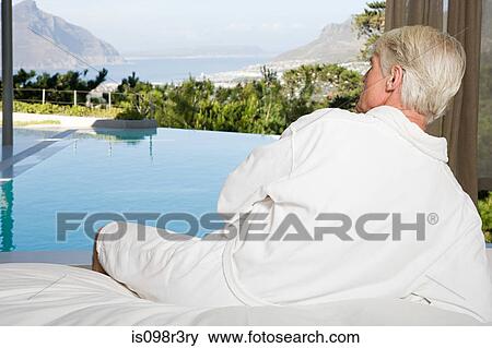 Middle aged man wearing bathrobe lying on bed and looking out at swimming pool View Large Photo Image Stock Photo - Middle aged man wearing bathrobe lying on bed and looking out at swimming pool. Fotosearch