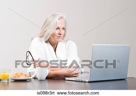 Middle aged woman sitting at breakfast table with laptop View Large Photo Image Stock Photograph - Middle aged woman sitting at breakfast table with laptop. Fotosearch