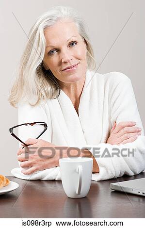 Stock Photography - Middle aged woman sitting at breakfast table in bathrobe. Fotosearch
