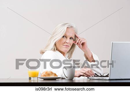 Stock Image - Middle aged woman using laptop at breakfast time. Fotosearch