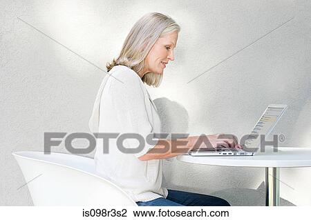 Stock Image - Middle aged woman using laptop. Fotosearch