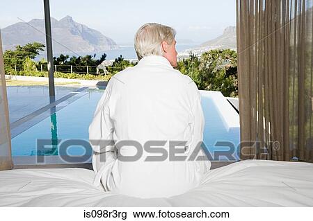 Rear view of middle aged man sitting on bed with view out to swimming pool View Large Photo Image Stock Image - Rear view of middle aged man sitting on bed with view out to swimming pool. Fotosearch