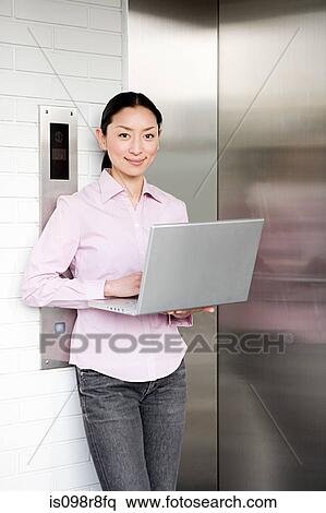 Woman using a laptop computer outside elevator View Large Photo Image Stock Photography - Woman using a laptop computer outside elevator. Fotosearch