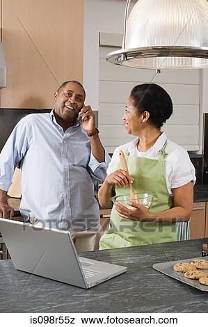 Stock Photo - Couple in kitchen with laptop and cellphone. Fotosearch