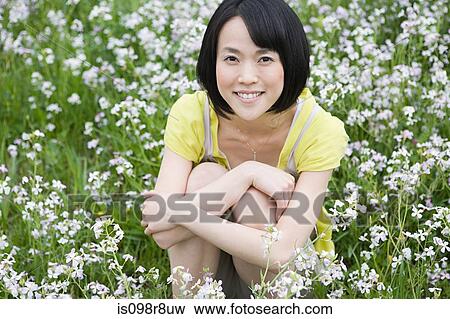 Stock Photo - Young woman sitting in field of flowers. Fotosearch