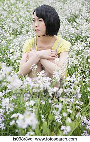 Stock Photography - Young woman sitting in field of flowers. Fotosearch