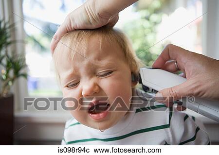 Stock Image - Adult putting thermometer in ear of crying baby. Fotosearch