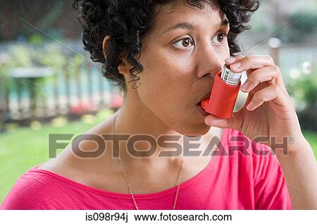 Stock Image - Woman taking asthma inhaler. Fotosearch