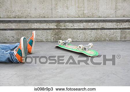 Stock Image - Feet of teenager who has fallen off skateboard. Fotosearch