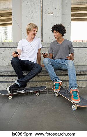 Picture - Teenage boys with cellphones and skateboards. Fotosearch