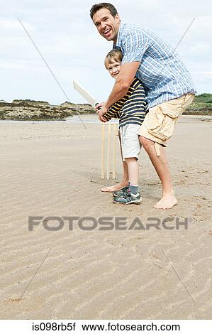 Stock Image - Father and son playing cricket on beach. Fotosearch