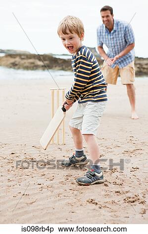 Stock Photography - Father and son playing cricket on beach. Fotosearch