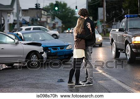 Stock Image - Young couple looking at crashed cars. Fotosearch