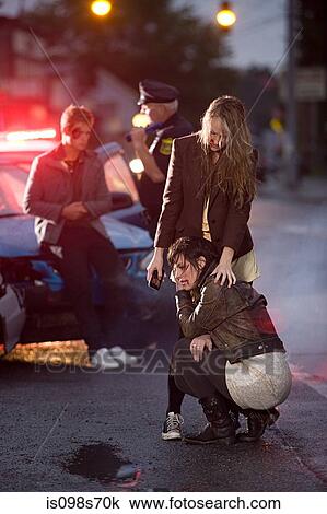 Stock Image - Young people and police officer at scene of car crash. Fotosearch