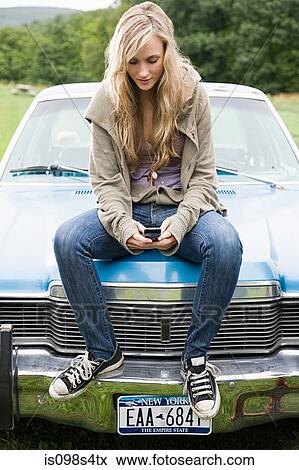 Young woman sitting on car with cellphone View Large Photo Image Stock Photo - Young woman sitting on car with cellphone. Fotosearch
